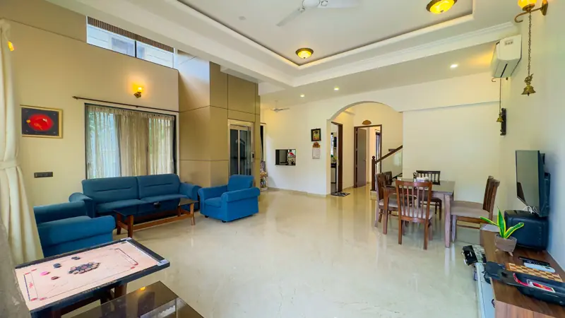 Bright double-height living room with blue sofas and a carrom board